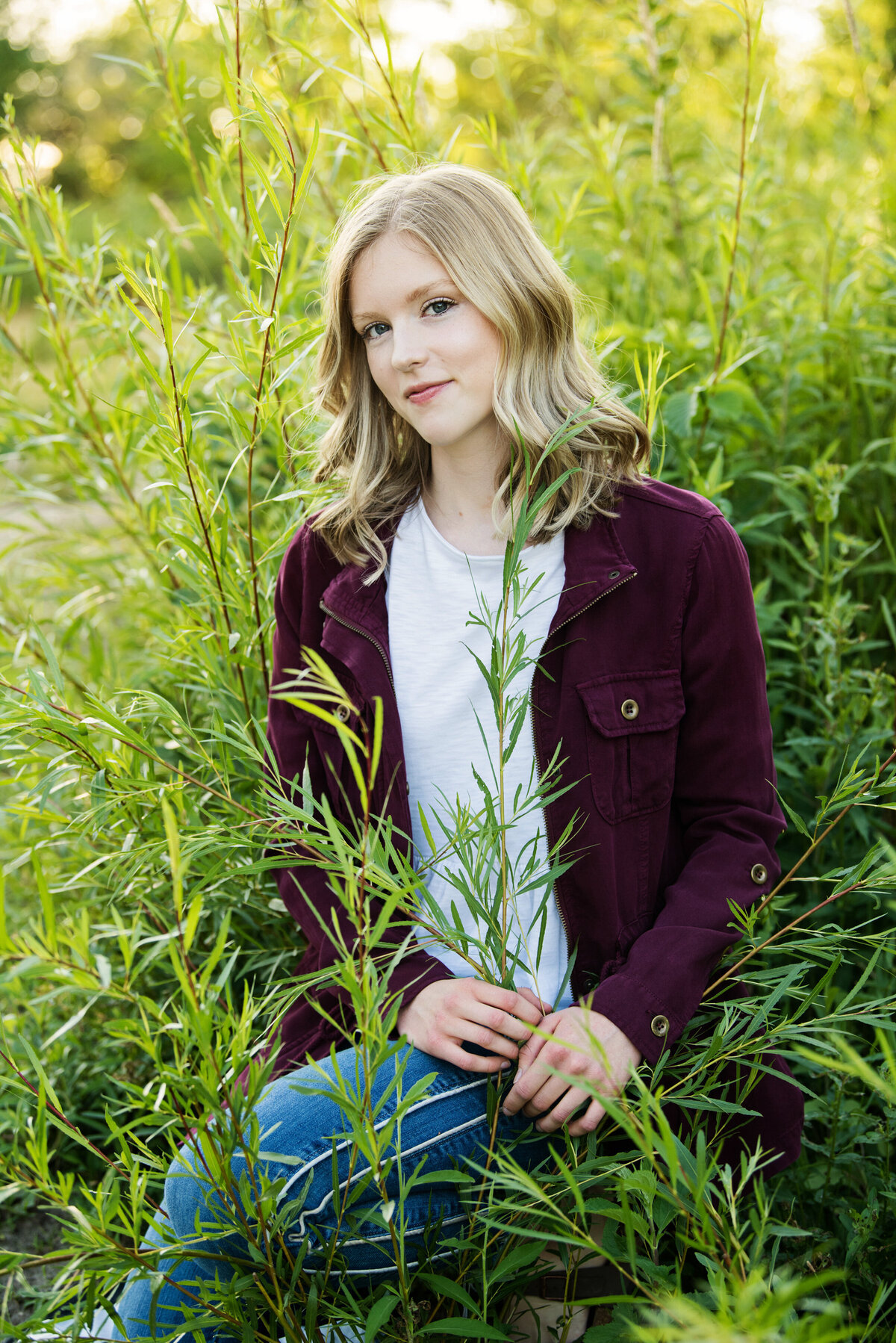 grad photo of girl with green willow branches wearing maroon jacket