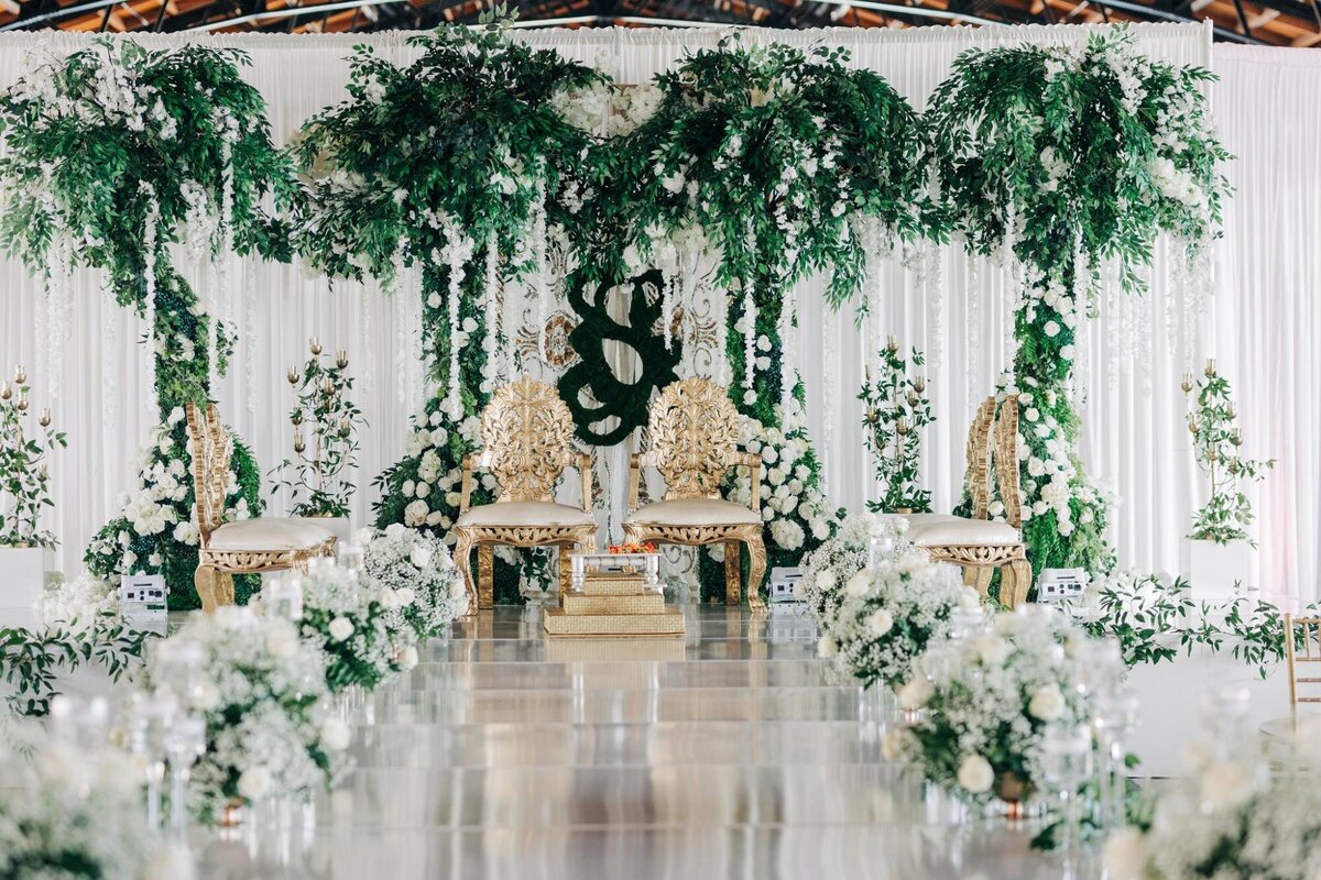 Elegant wedding venue decorated with white flowers and green foliage, featuring ornate chairs and floral arrangements.Elegant wedding venue decorated with white flowers and green foliage, featuring ornate chairs and floral arrangements.