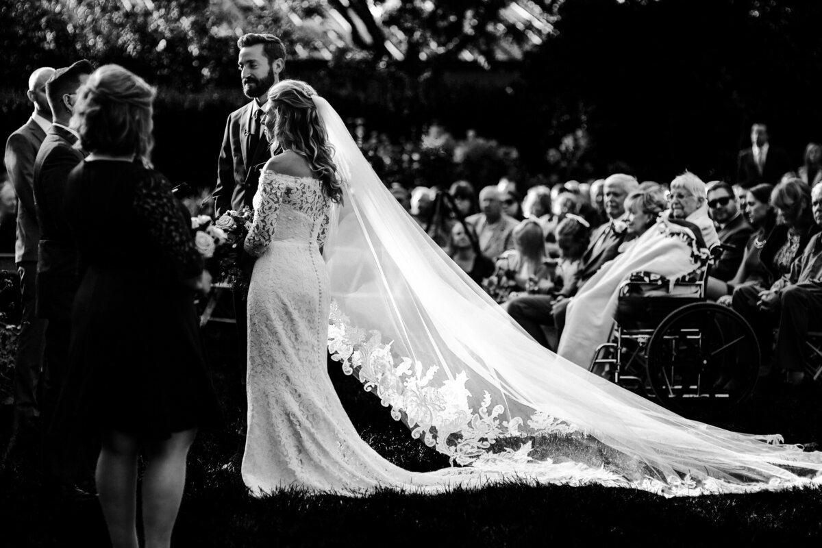 One of the top wedding photos of 2020. Taken by Adore Wedding Photography- Toledo, Ohio Wedding Photographers. This photo is of a wedding ceremony while grand parents watch on. The bride has a beautiful veil that is laid out behind her. The wedding took place at the Toledo Zoo