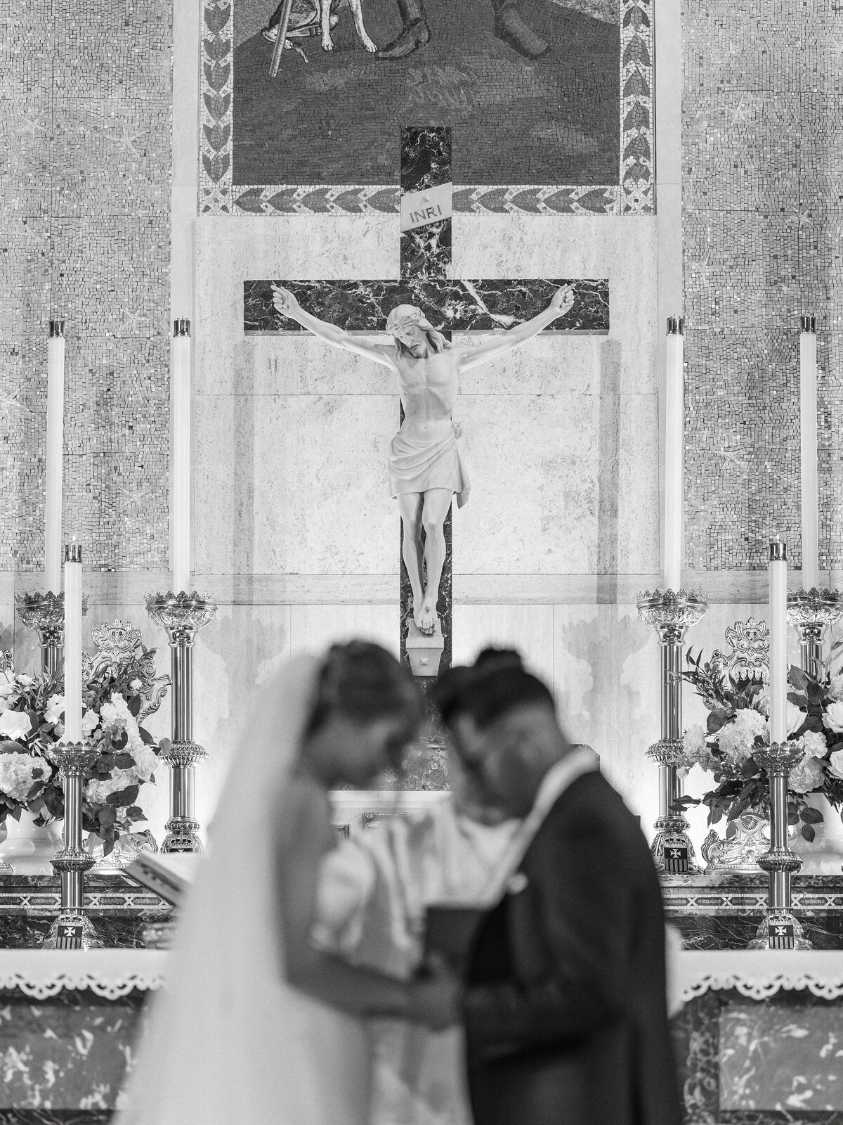 Bride and groom praying out of focus with Crucifix in focus over their heads at St Rocco Catholic Church wedding in Cleveland 