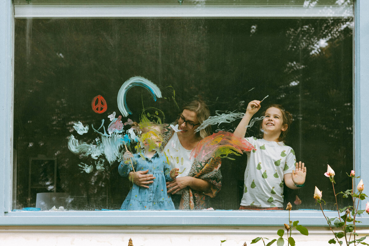 photo taken through window of mom with two kids painting on the glass