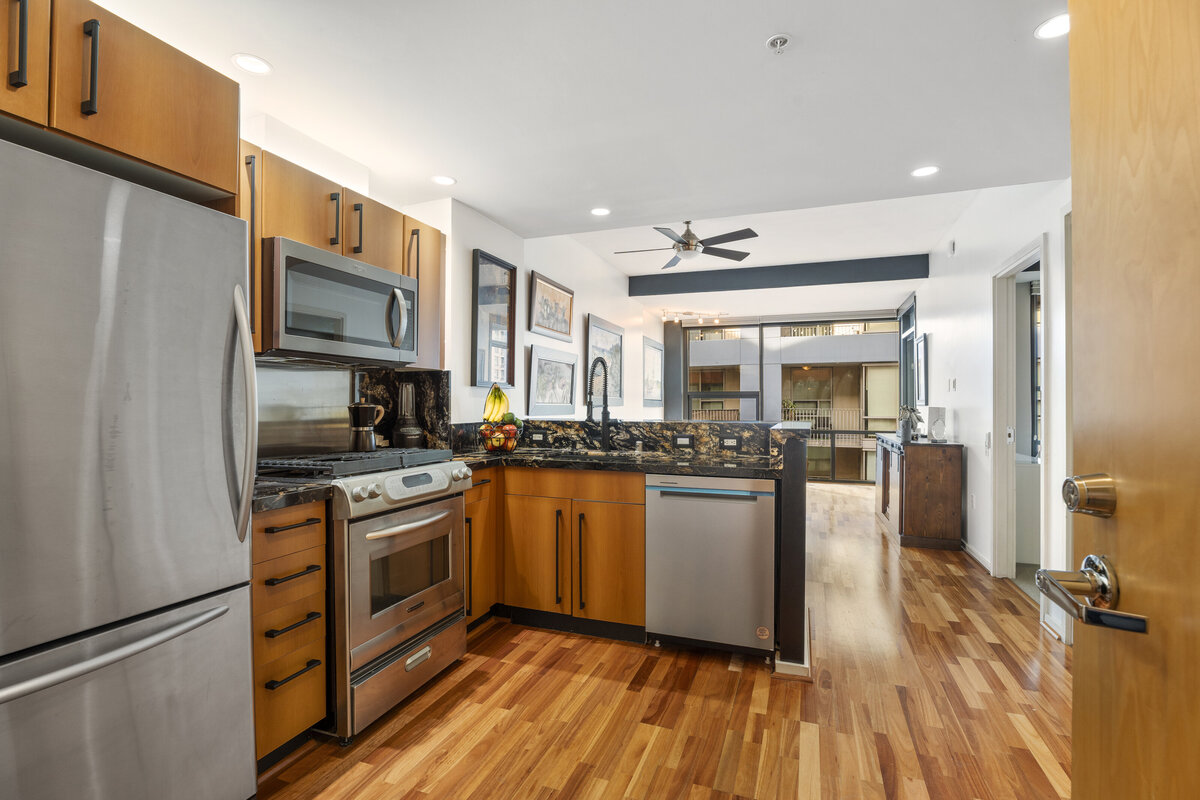 Narrow apartment in the Icon Building with wood floors and a modern kitchen. Looks out to a balcony with views of downtown San Diego.