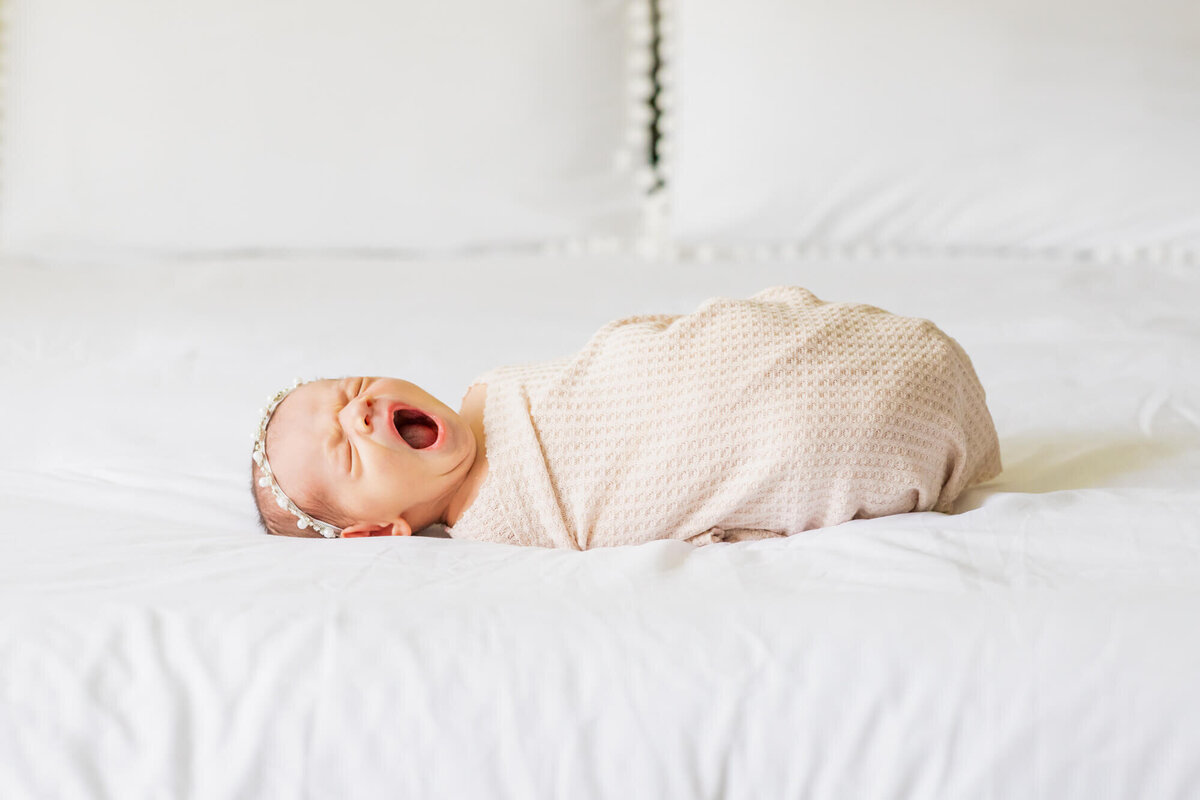 Newborn baby girl laying on a bed yawning
