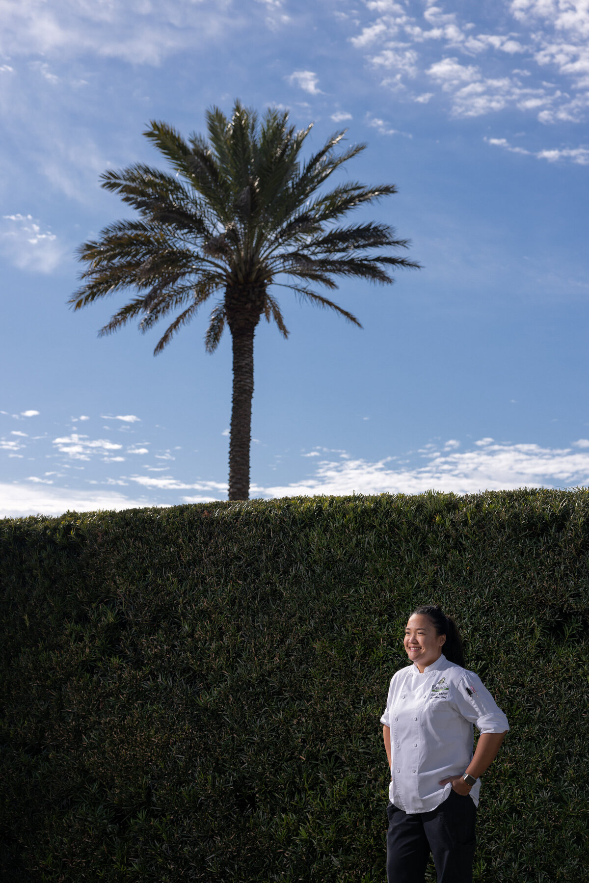 A chef standing outside next to a tall hedge