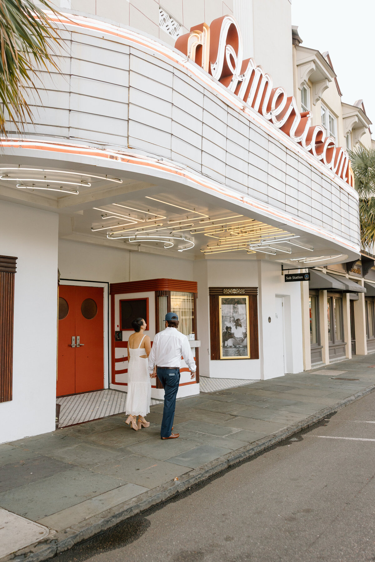 Couple walking into American theater in downtown Charleston during a playful and stylish couples session.