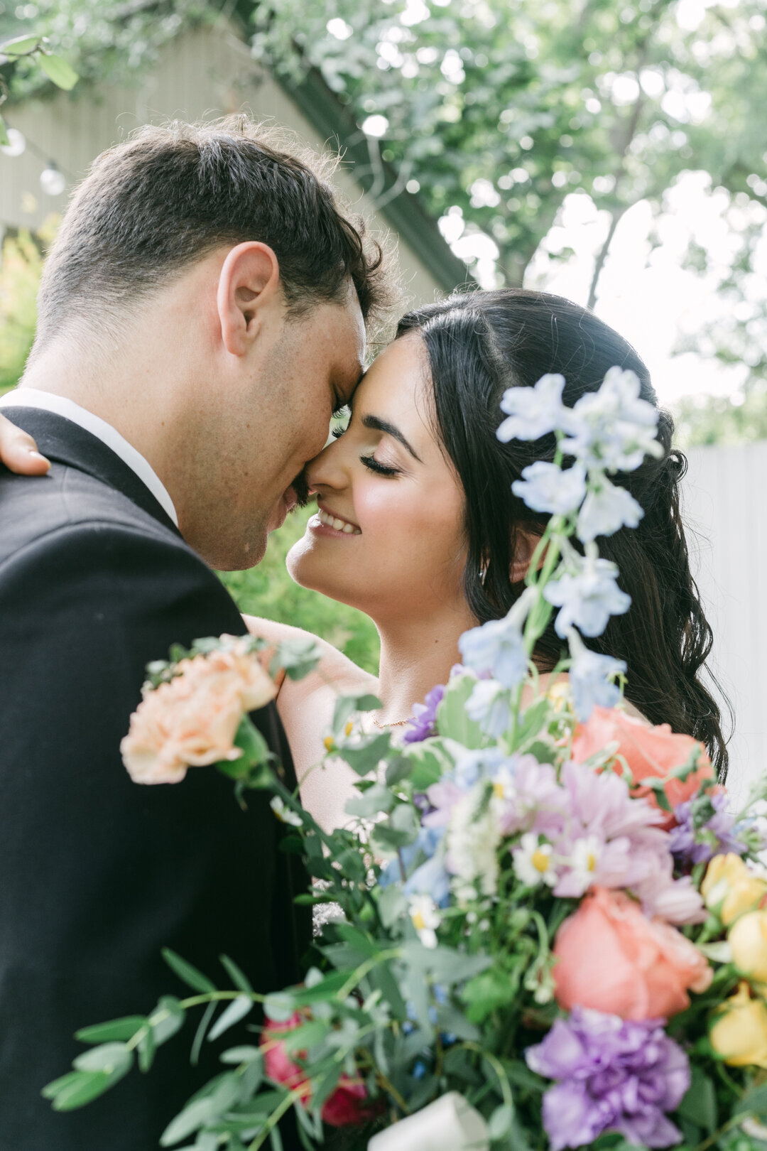 Bride and groom sharing a sweet kiss with pastel floral bouquet and greenery at a garden ceremony in Austin, Texas Hill Country, coordinated by Marla Weddings.