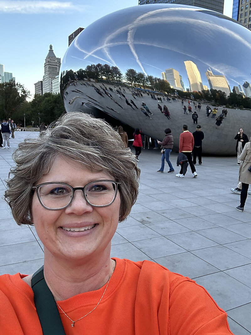 Before image of client smiling outdoors near reflective sculpture, wearing an orange sweatshirt, taken before her dating photo experience with Shannon Kathleen Photography