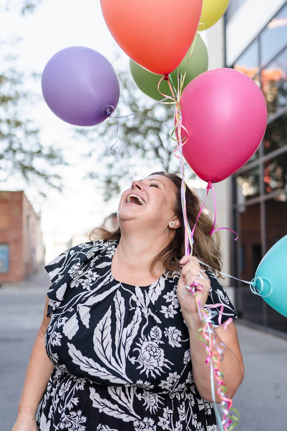 joyful woman in a black and white dress looking up at colourful balloons