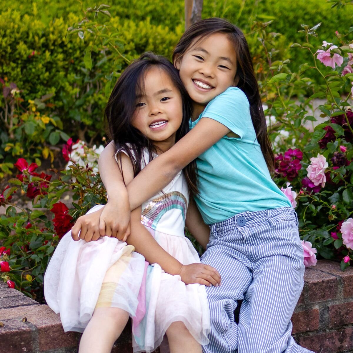 Sisters hugging on a brick wall surrounded by flowers during Bay Area school photography lifestyle session – Ellobelle Photography