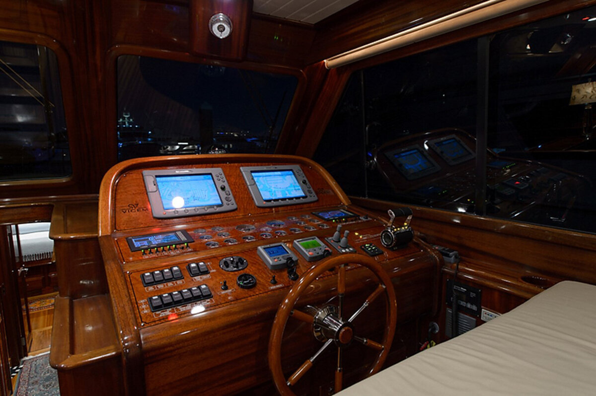 wooden cockpit of a yacht at night, featuring a variety of navigational instruments, including multiple screens and buttons
