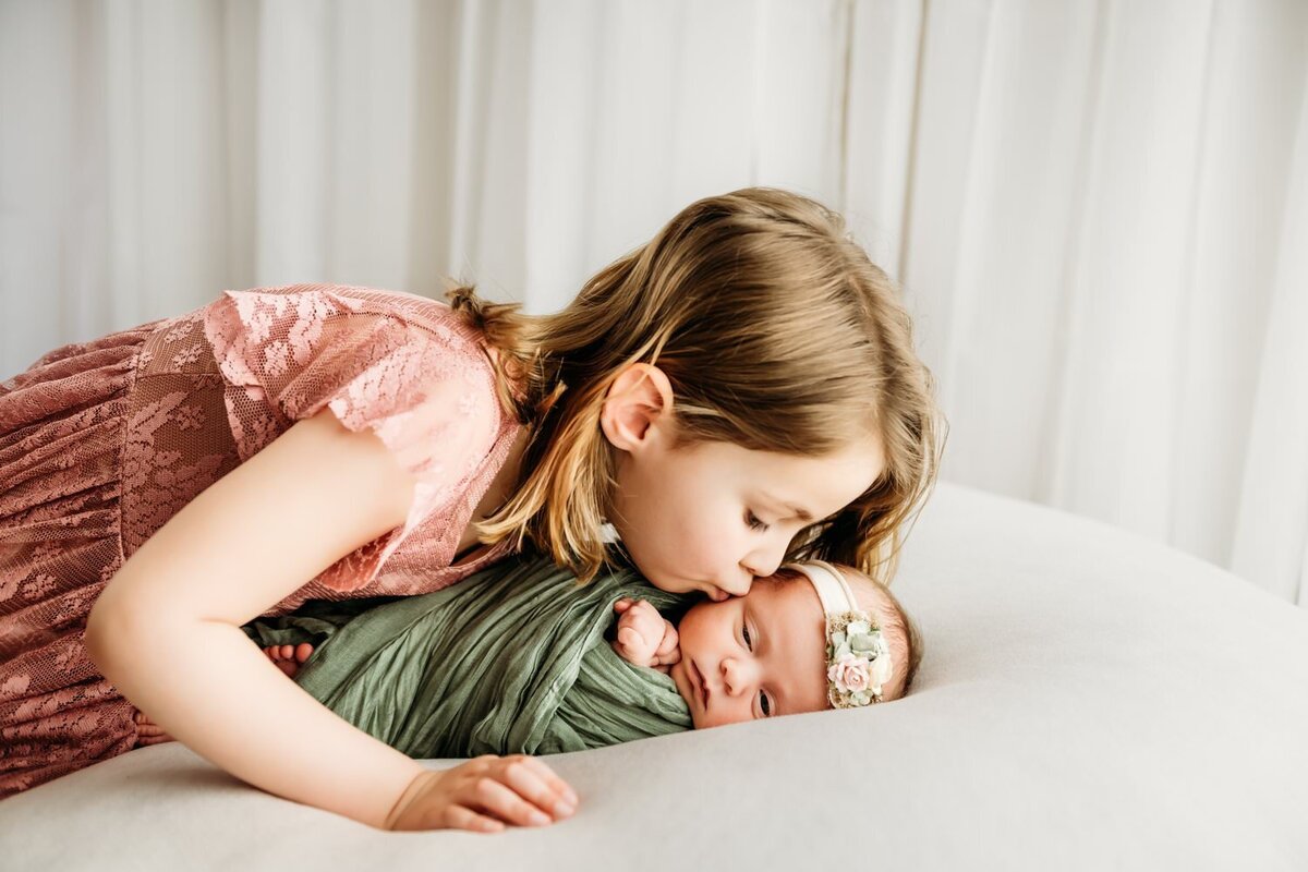 baby kissed by big sister during studio photography session in martinez.