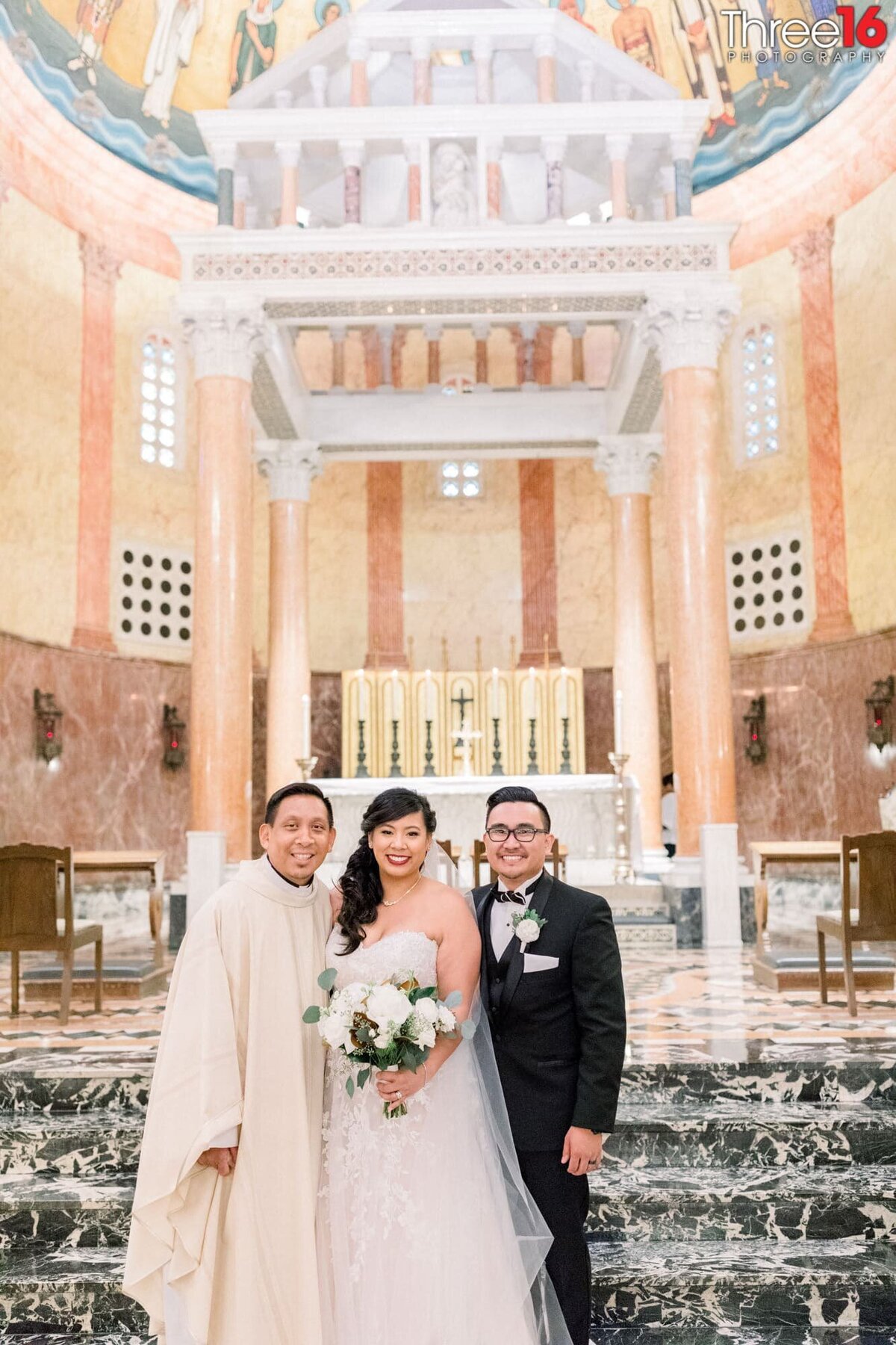 Bride and Groom pose for a photo with the priest inside the church