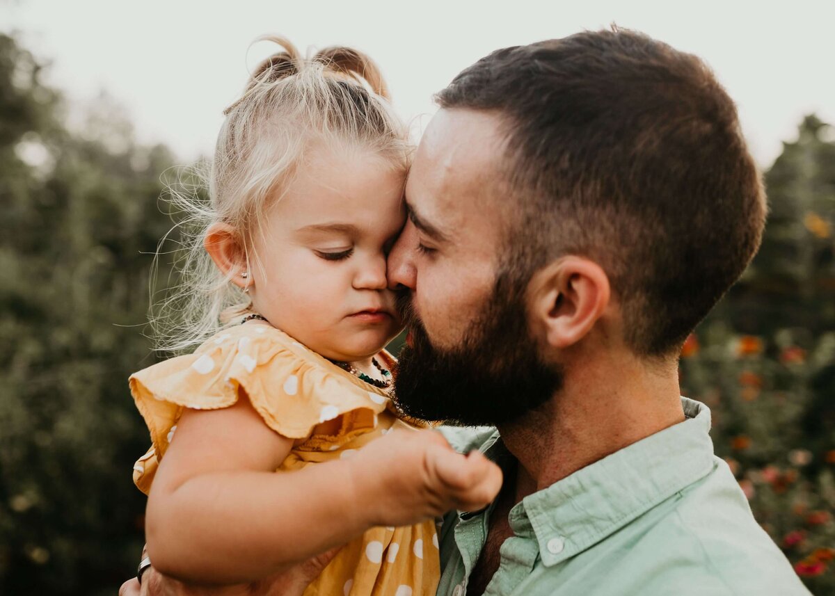 A father kisses his daughter in a field, captured by a Pittsburgh family photographer.