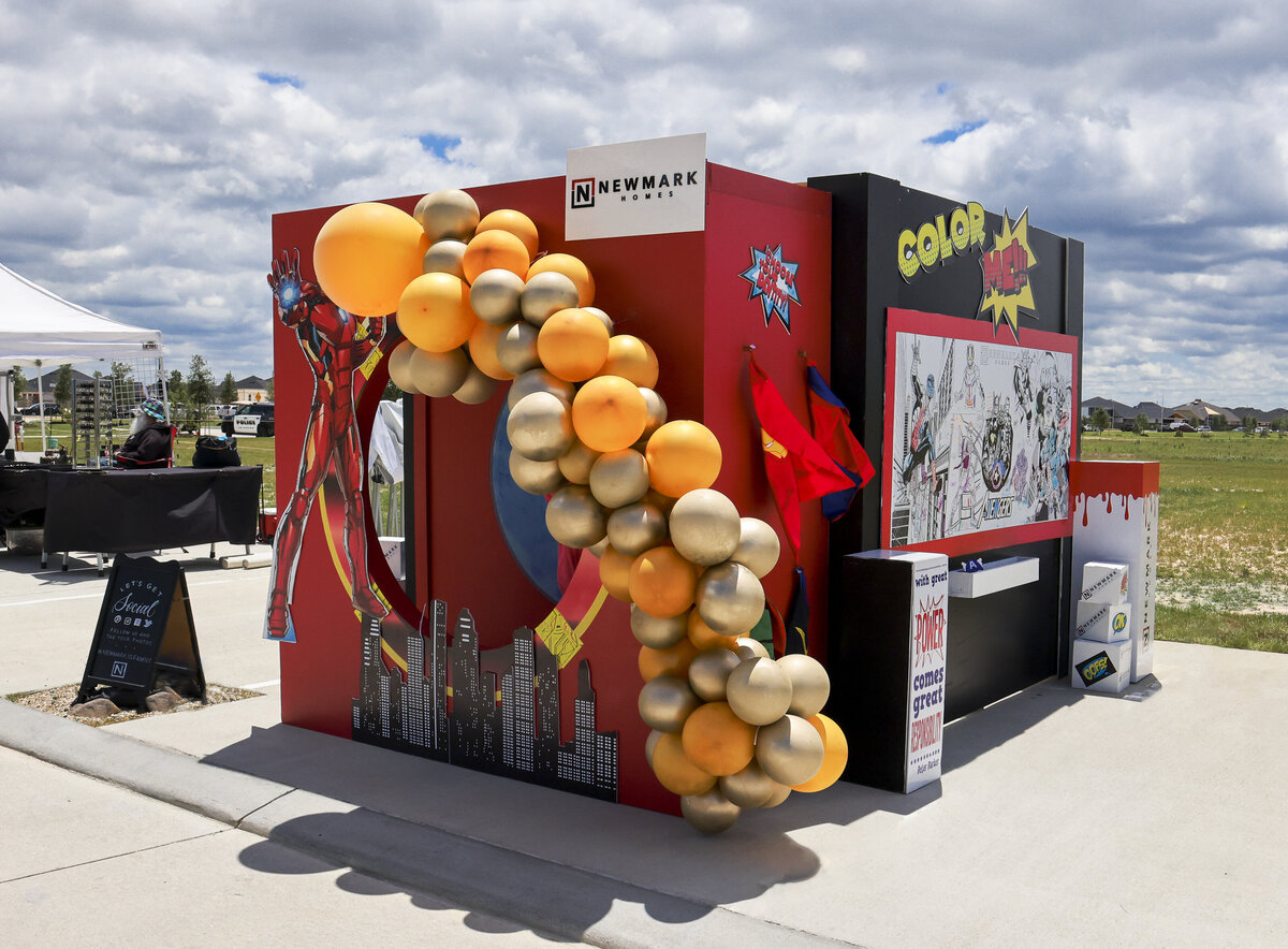 Superhero themed backdrop design for Newmark Homes with orange and gold balloon arch