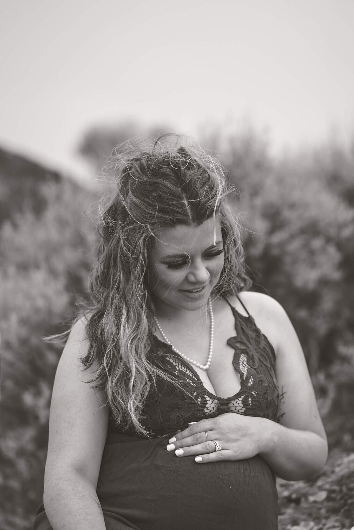 A beautiful woman smiles while holding her pregnant belly. Black and white image taken by Brittany Danielle Photography in Kamloops