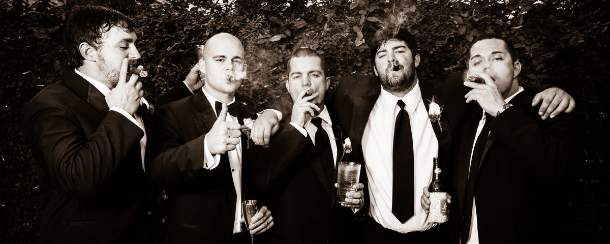A groom and his groomsmen smoking cigars at the wedding reception.
