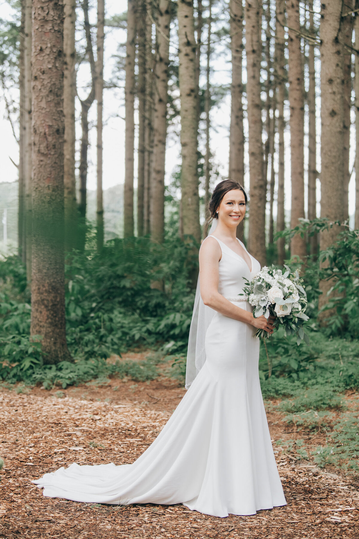 An elegant bride in a sleek white wedding dress holding a big, beautiful wedding bouquet