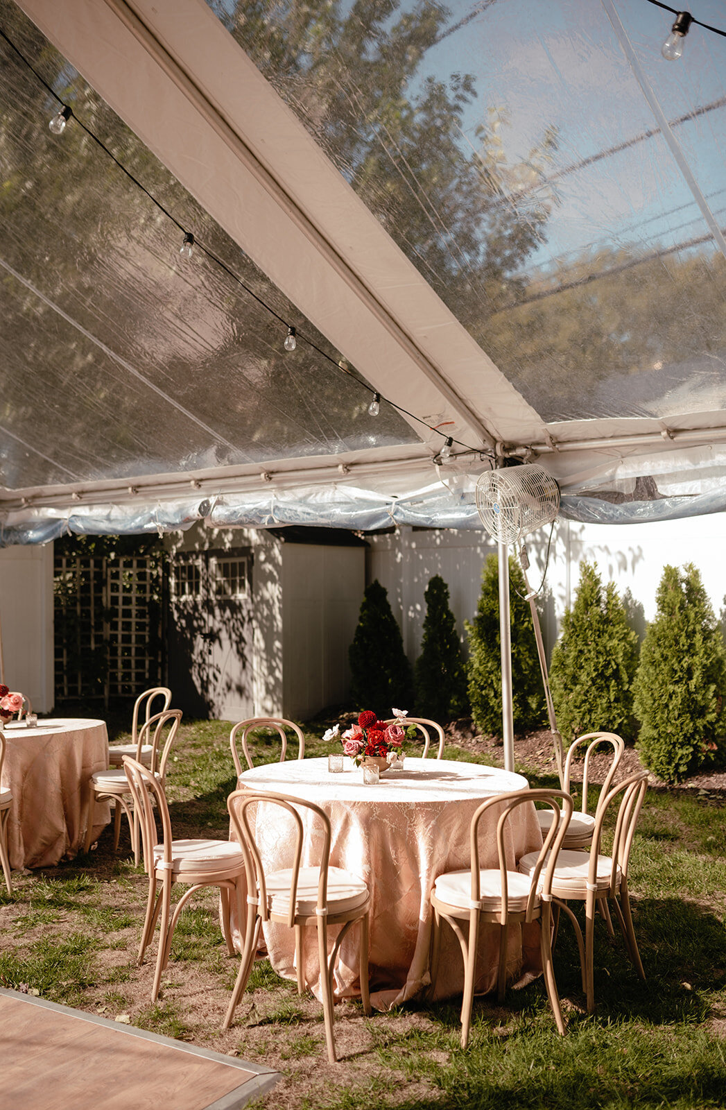A picturesque garden wedding setting with elegant round tables, wooden chairs, and floral centerpieces enhancing the outdoor atmosphere.