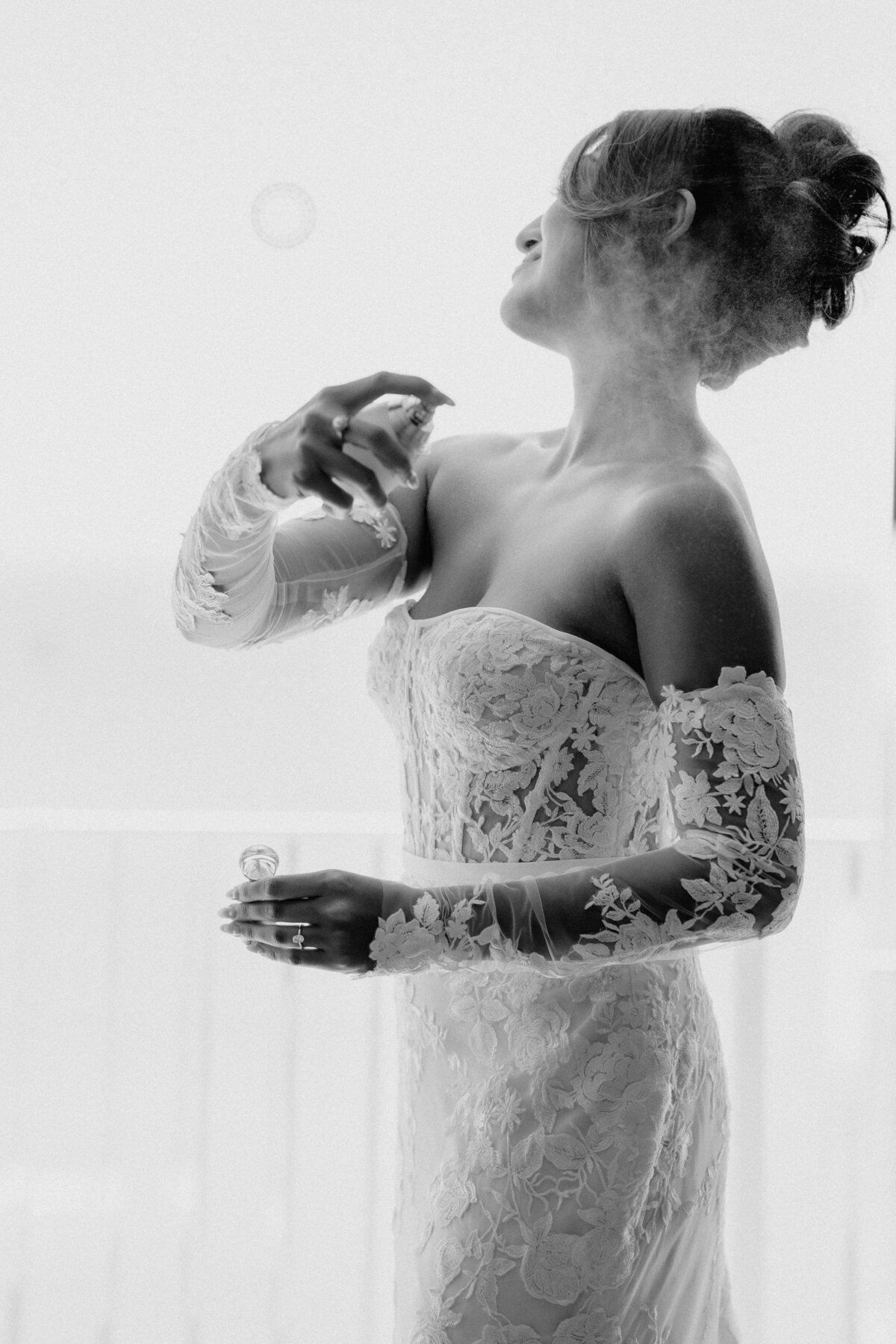 Bride applying perfume in front of window, spray can be seen