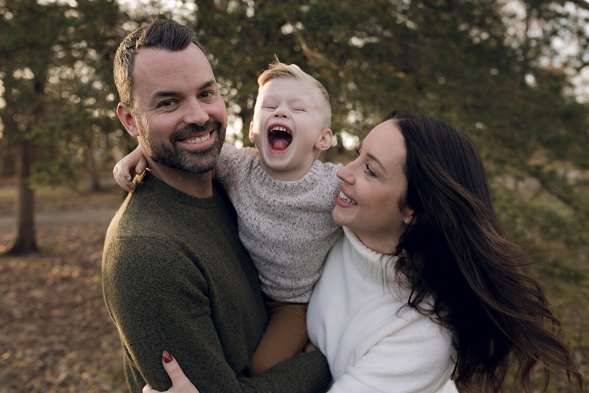 A heartwarming moment of parents and a child laughing outdoors, captured in an elegant documentary photography style.