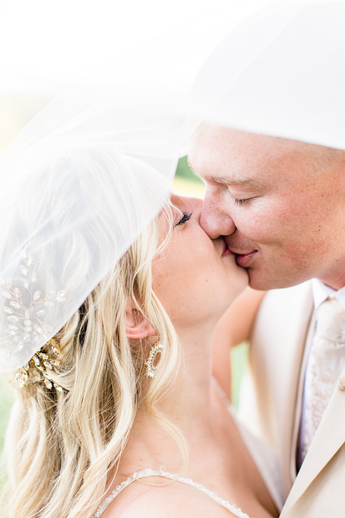 close-up of bride and groom kissing with her veil in the background
