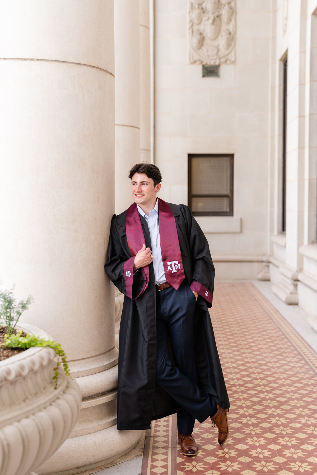 Texas A&M senior guy leaning on column and holding stole while wearing gown and stole and looking away while in columns of Administration Building