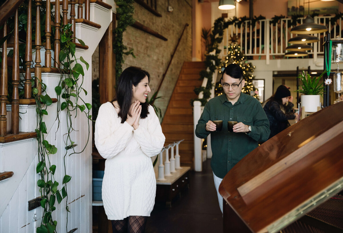 coffee shop engagement pictures in downtown Richmond with man holding two mugs of coffee as he walks to find a table with woman in a white dress