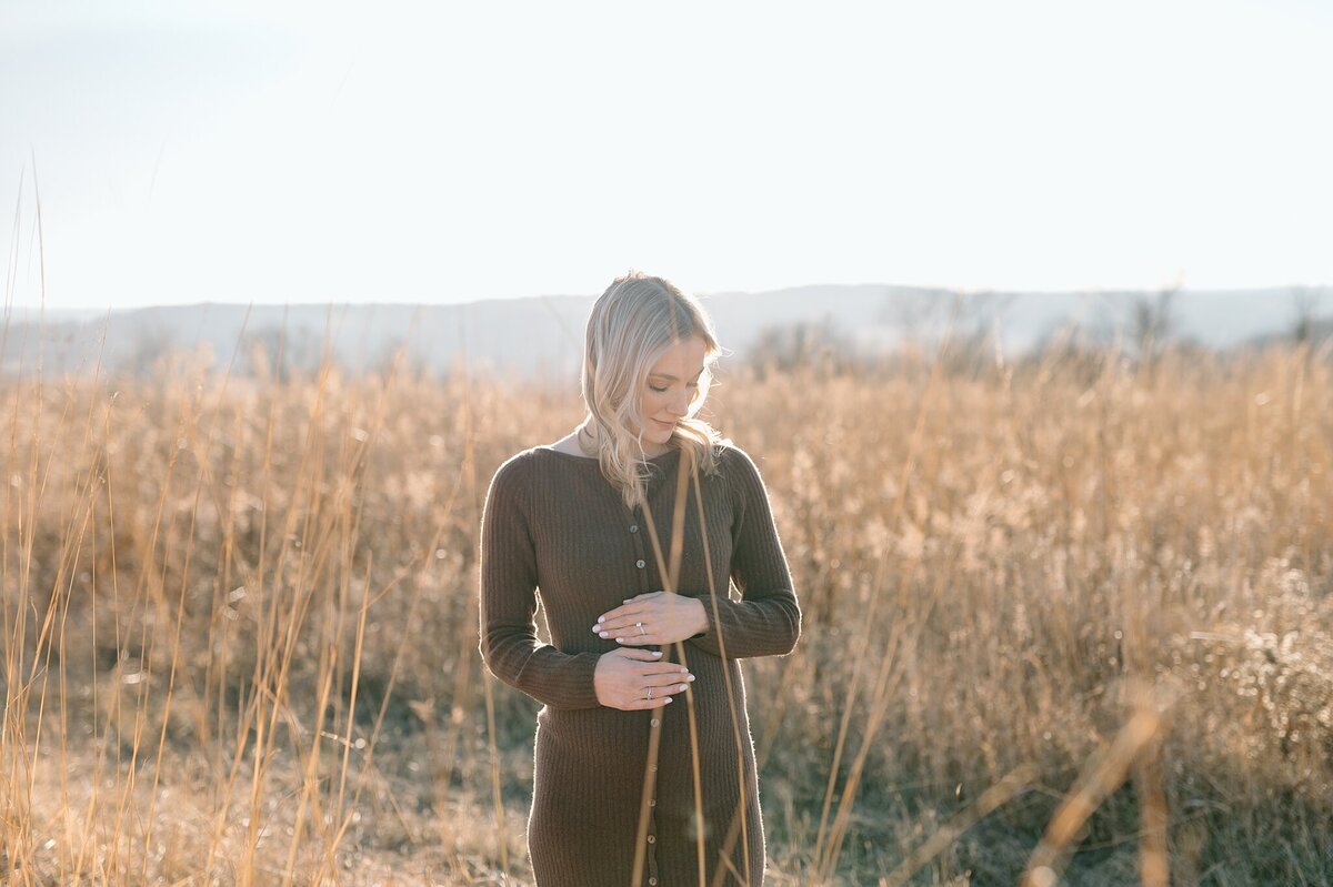 Mom-to-be gazing down toward pregnant belly in a Wisconsin field