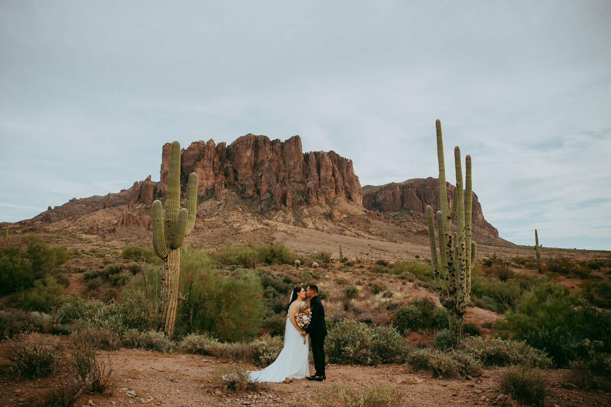 bride and groom stand between saguaro cacti