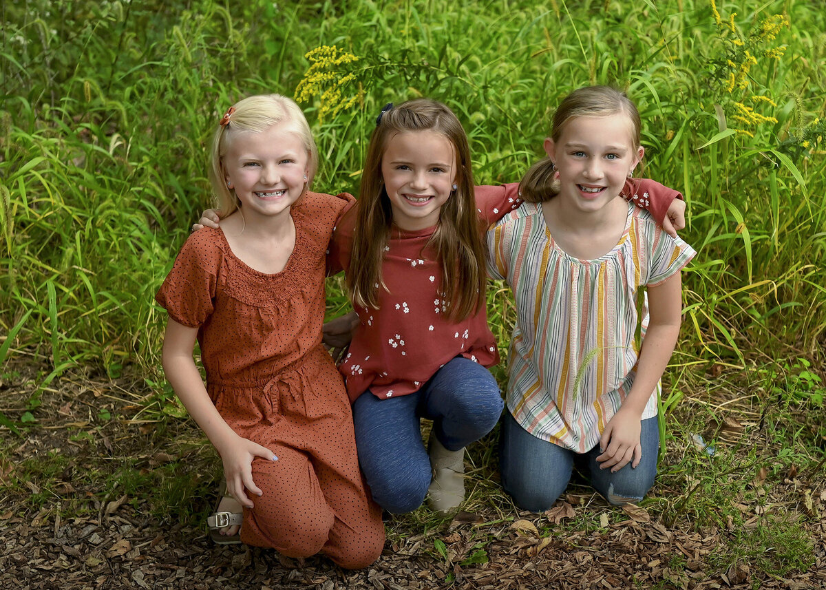3 girls kneel with their arms around each other smiling