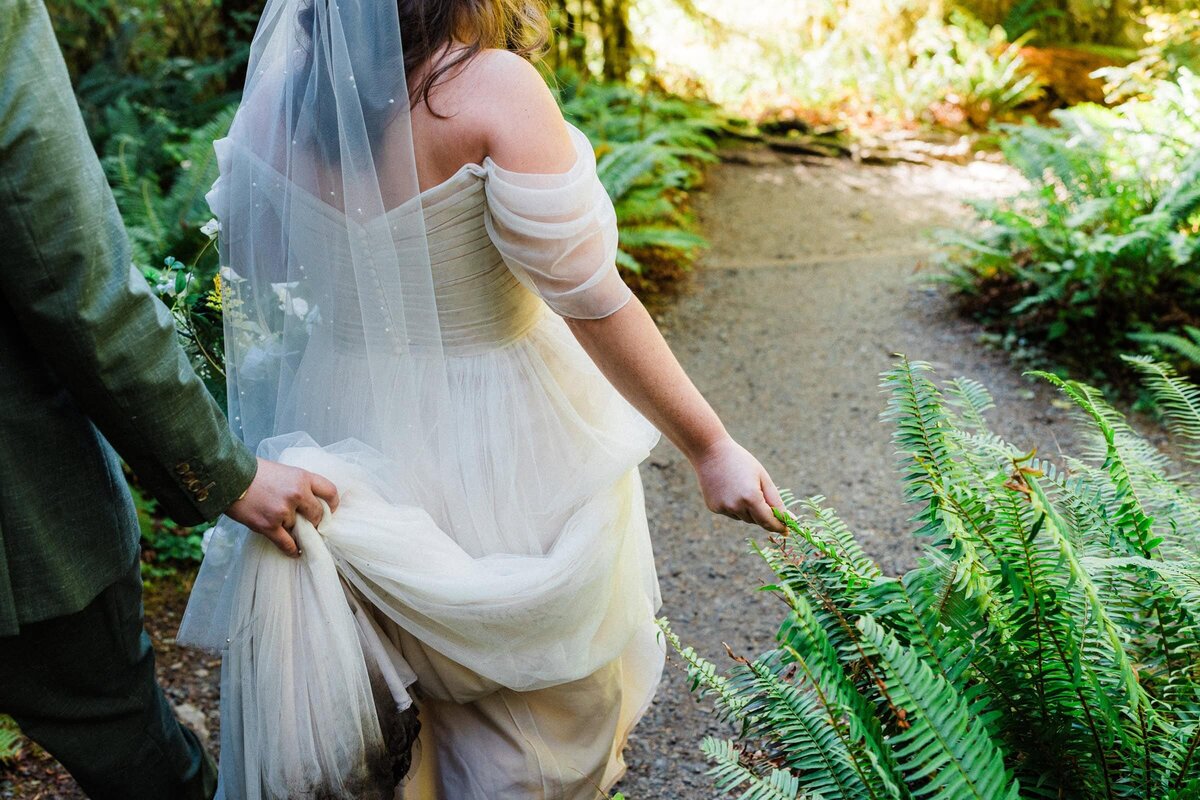 bride holding a fern plant on a hiking trail in the Hoh rainforest.