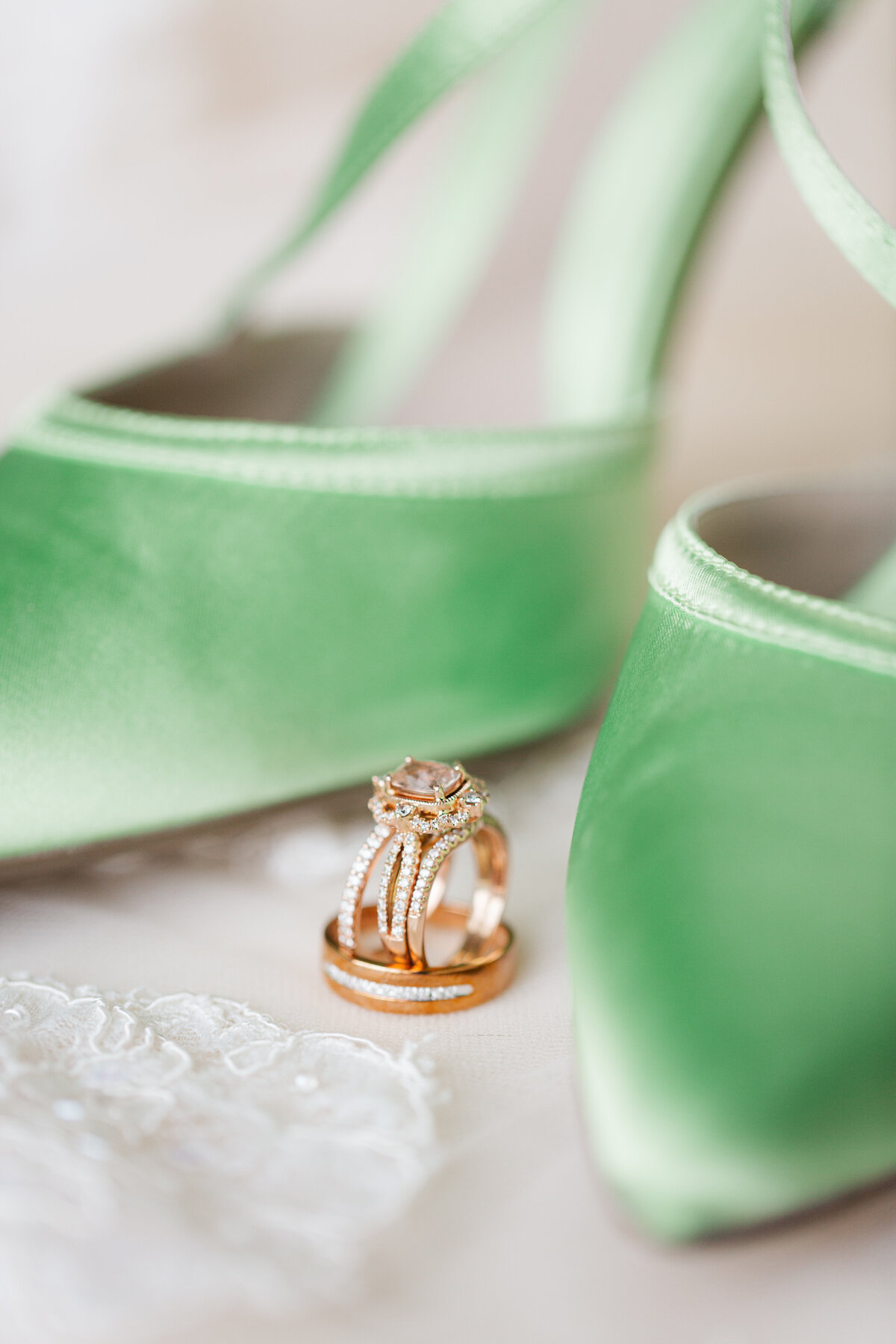 green satin wedding shoes with rose gold wedding rings nestled between them