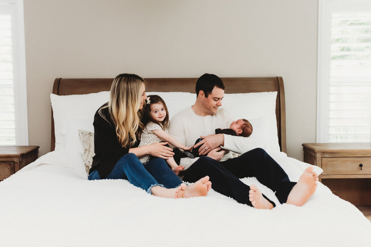Family sit on bed holding newborn baby boy