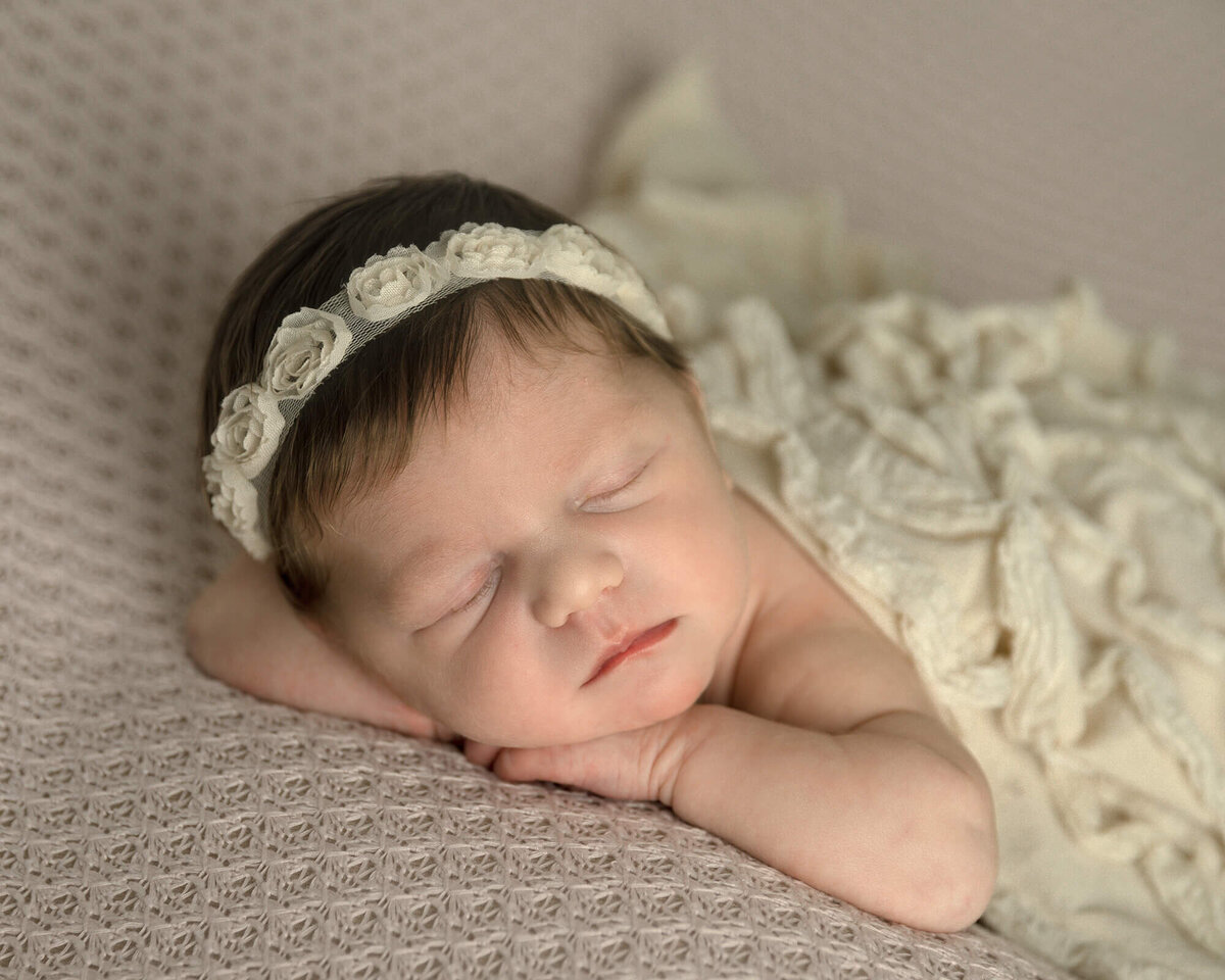 Newborn girl on pink fabric laying forward on her hands. Cream ruffle wrap covering her.