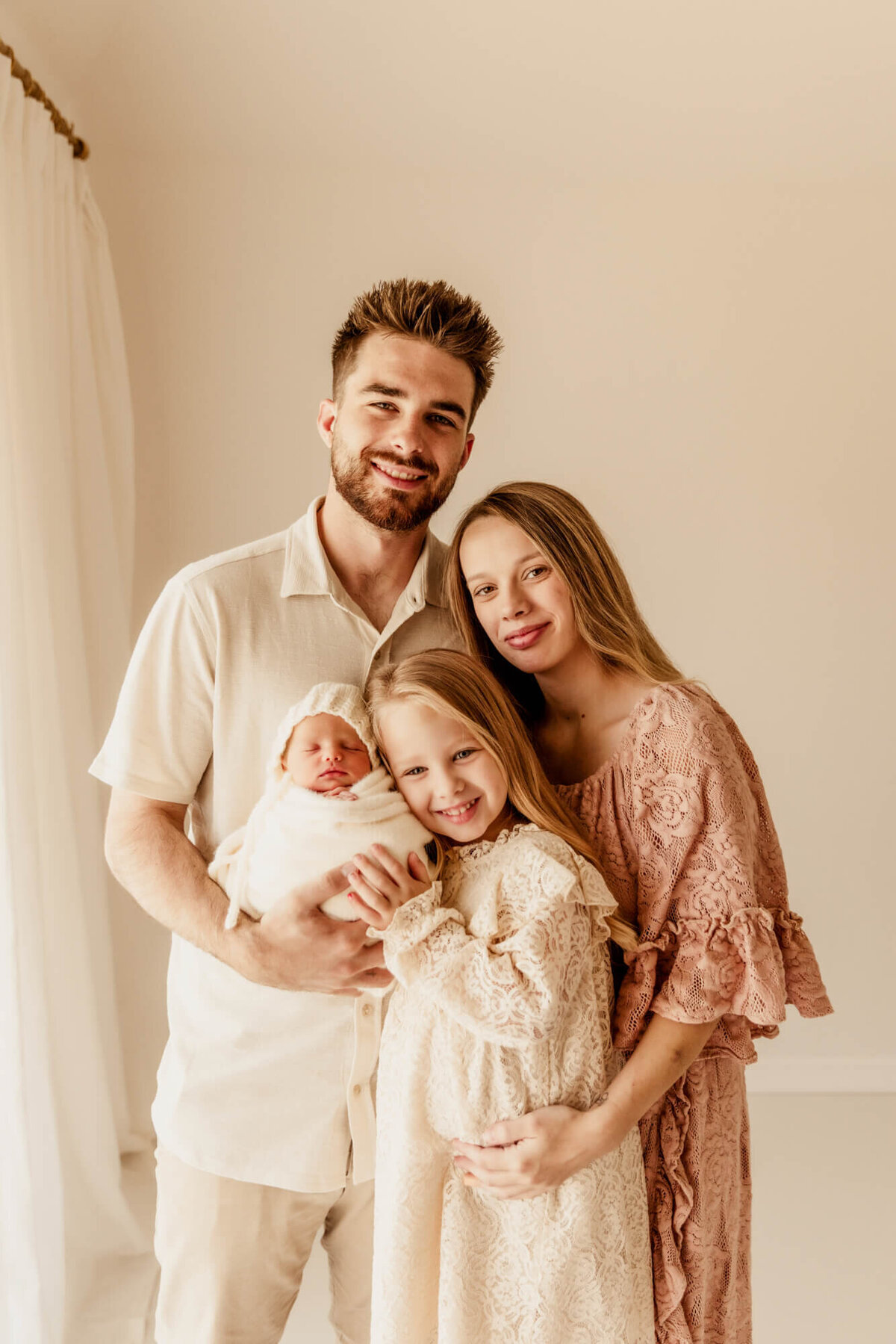 Family of four including a father, mother and two daughters smiling for a newborn photo session in Oklahoma City.