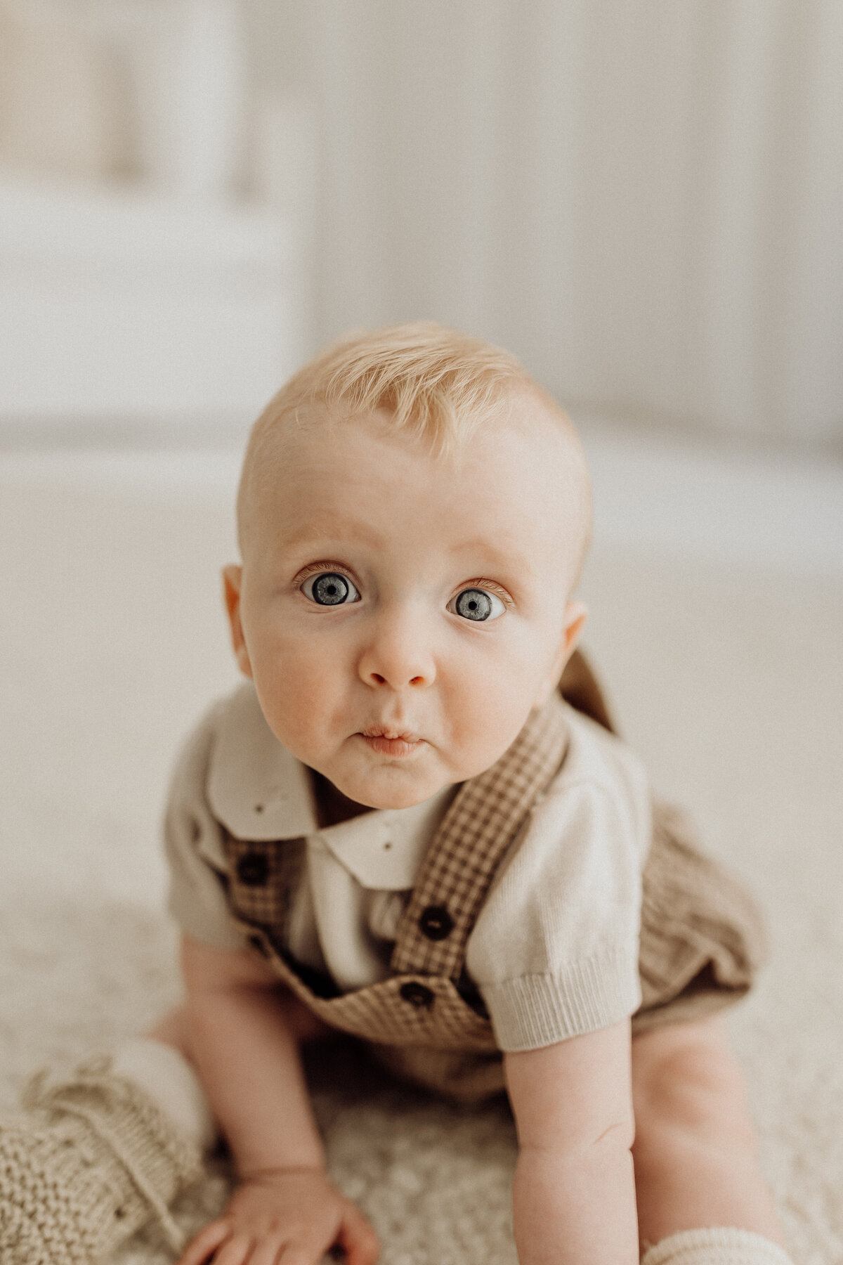 A little baby pulling super cute facials at the camera while lucy jane photography takes his milestone photographs