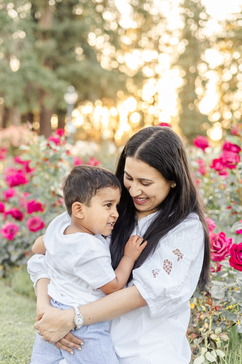 Mom and her toddler son lovingly hug each other during their photoshoot in the blooming rose garden in San Jose