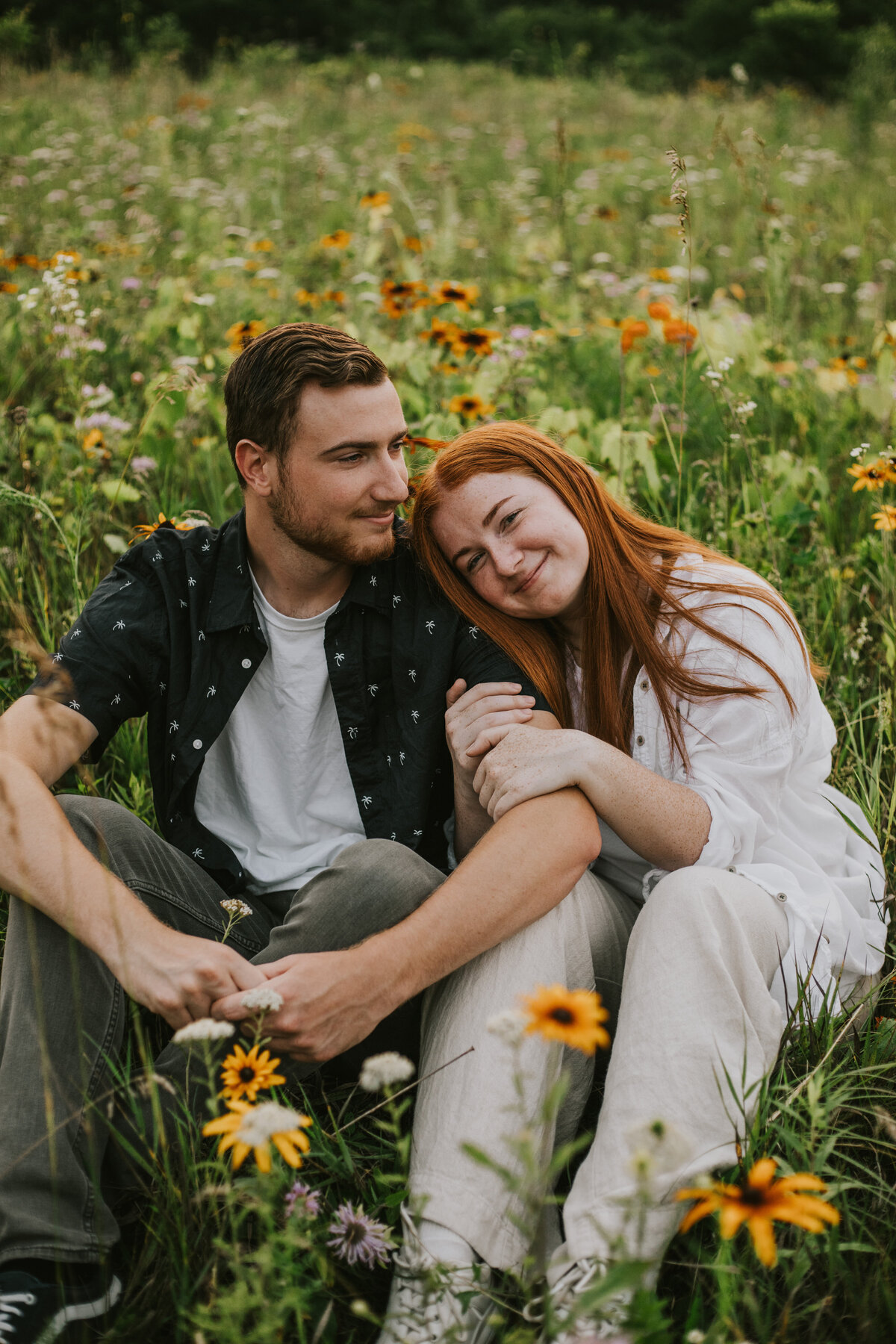 Engaged couple sitting in wildflowers, candid Indiana engagement session.