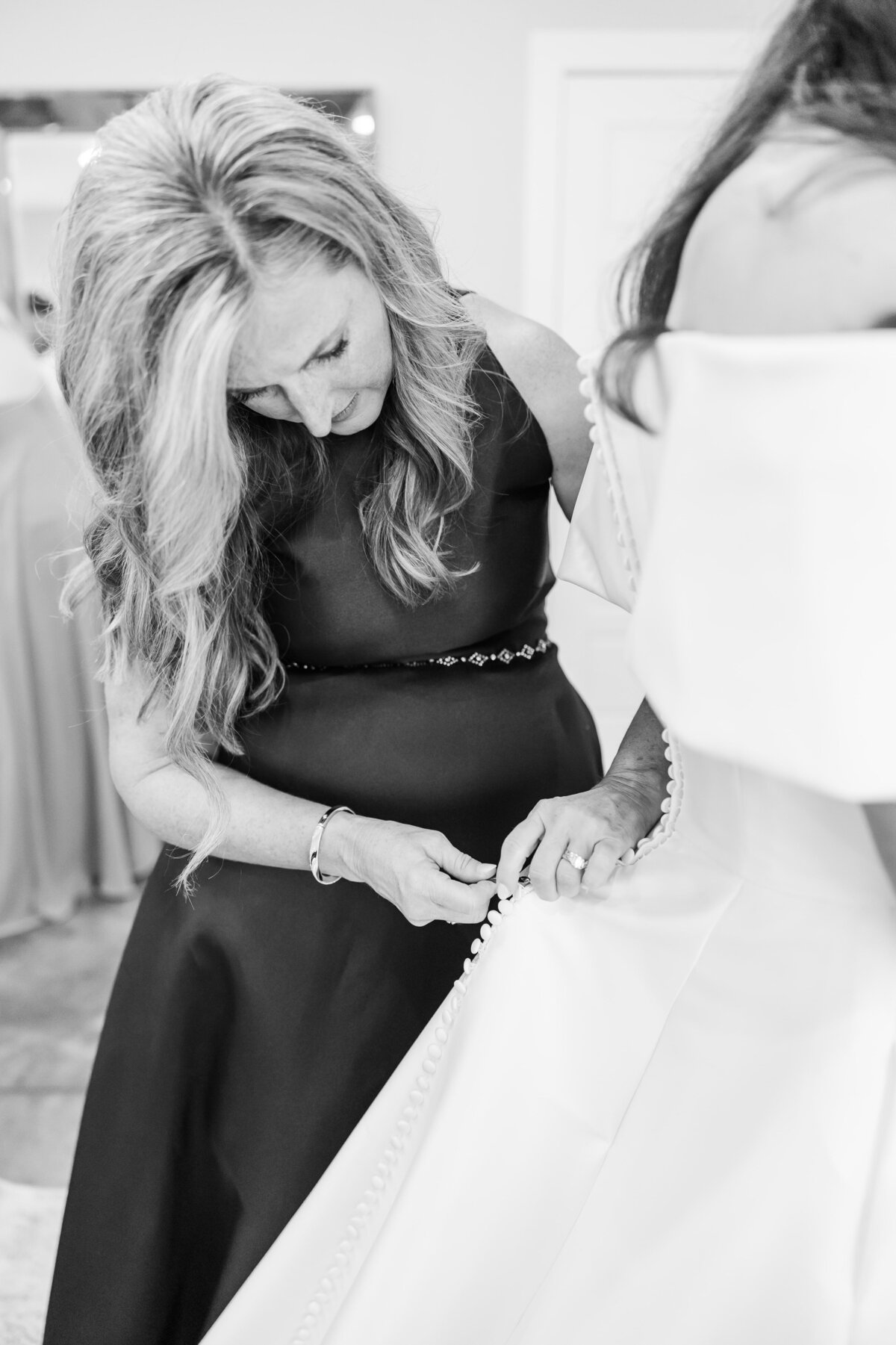 A mom buttons the bride into her dress in getting ready room
