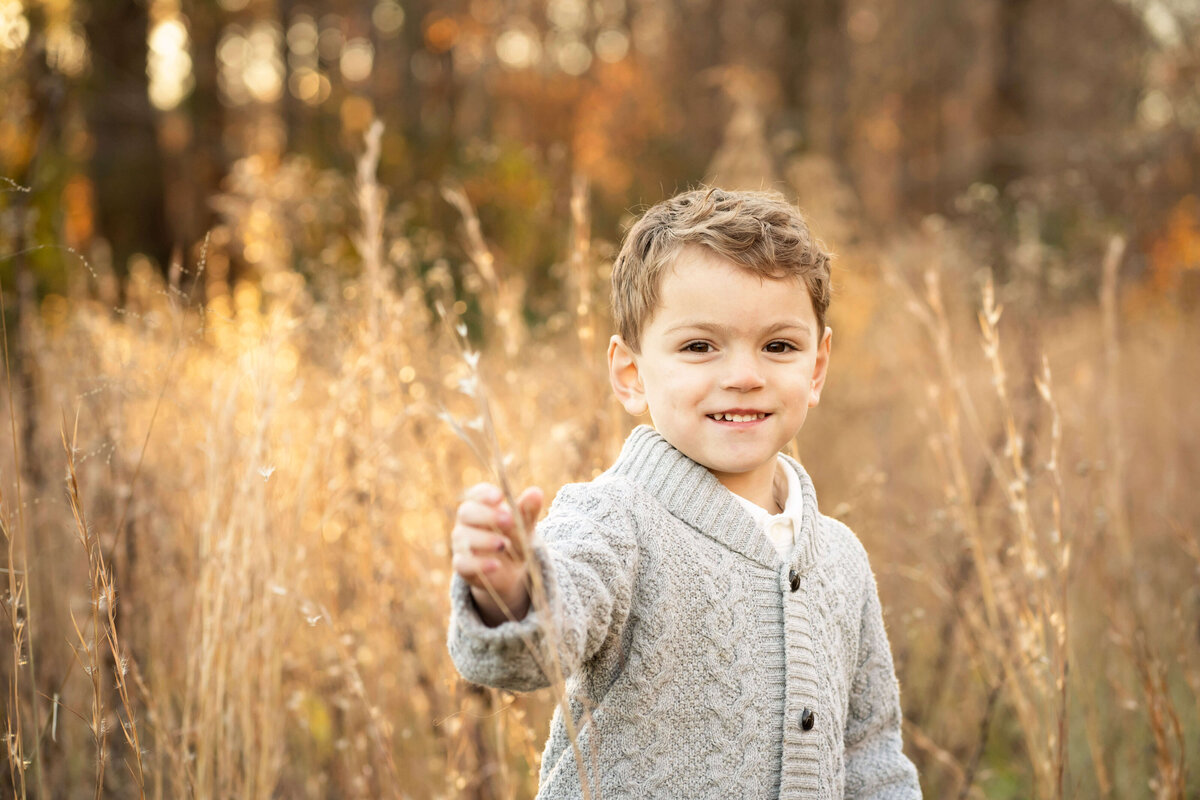 Young boy standing in field of tall grass and smiling at the camera