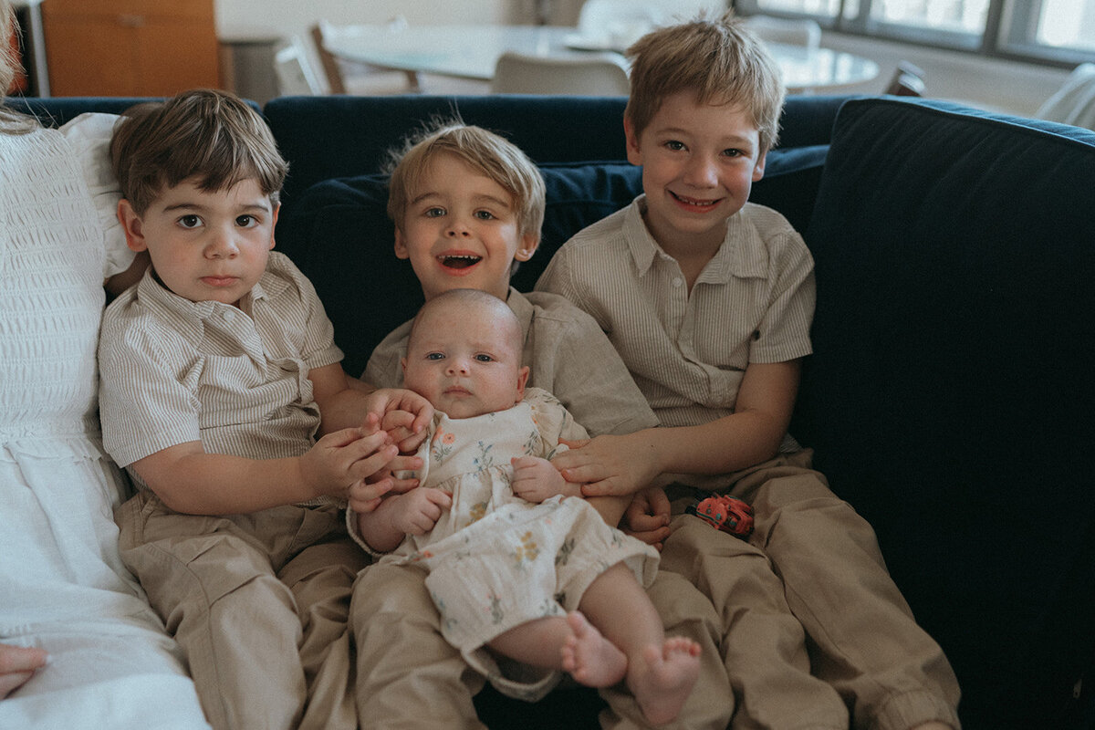 three kids smiling holding baby on couch during family newborn photoshoot captured by NYC newborn photographer Elsie Goodman 