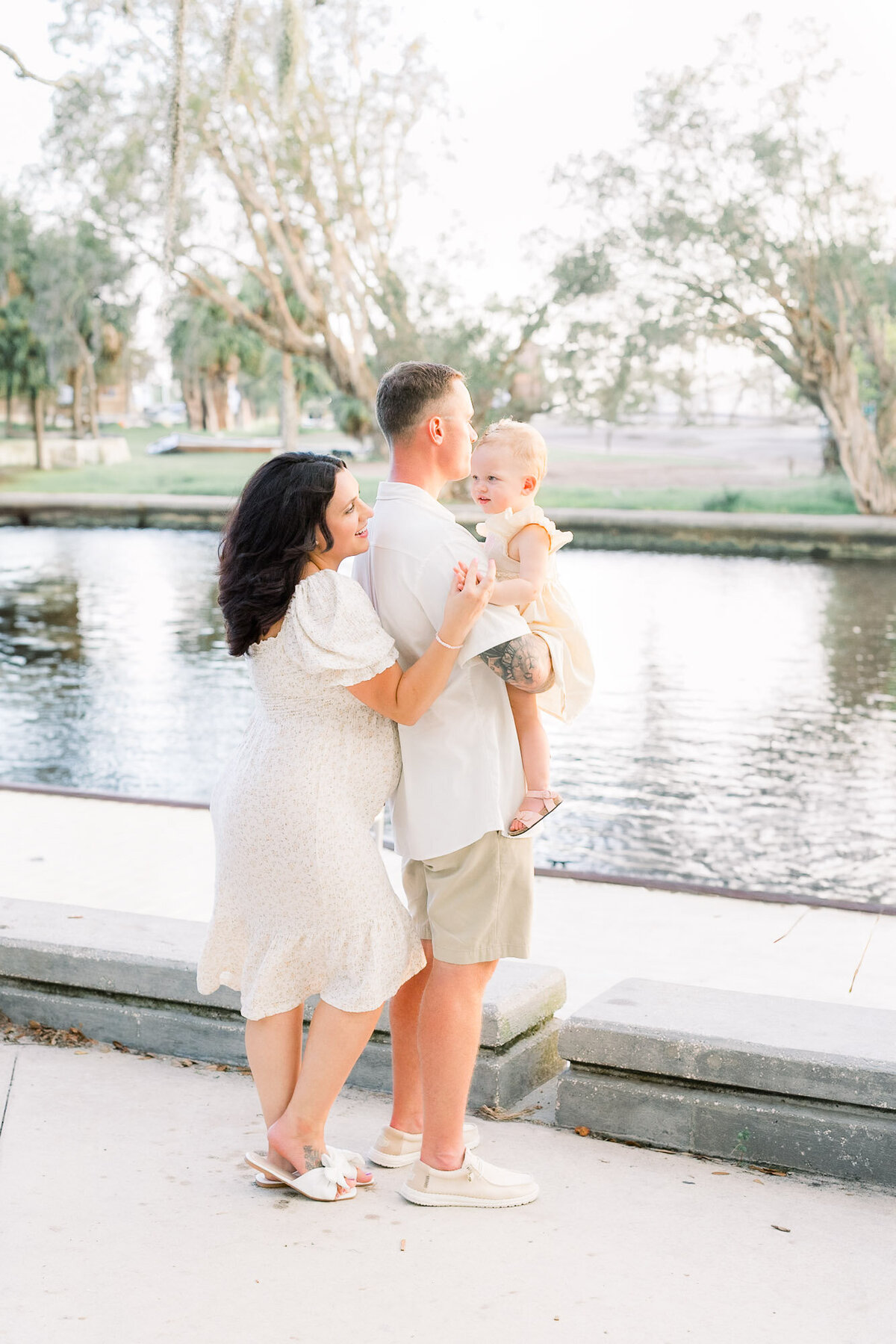 Pregnant couple holding toddler watching sunset by the river for a Tampa maternity photographer Tina Marie Studio.