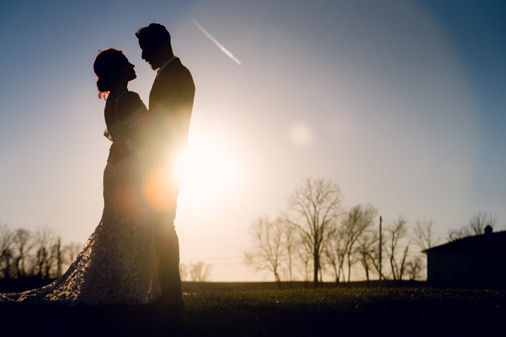 A bride and groom are silhouetted against the sun.