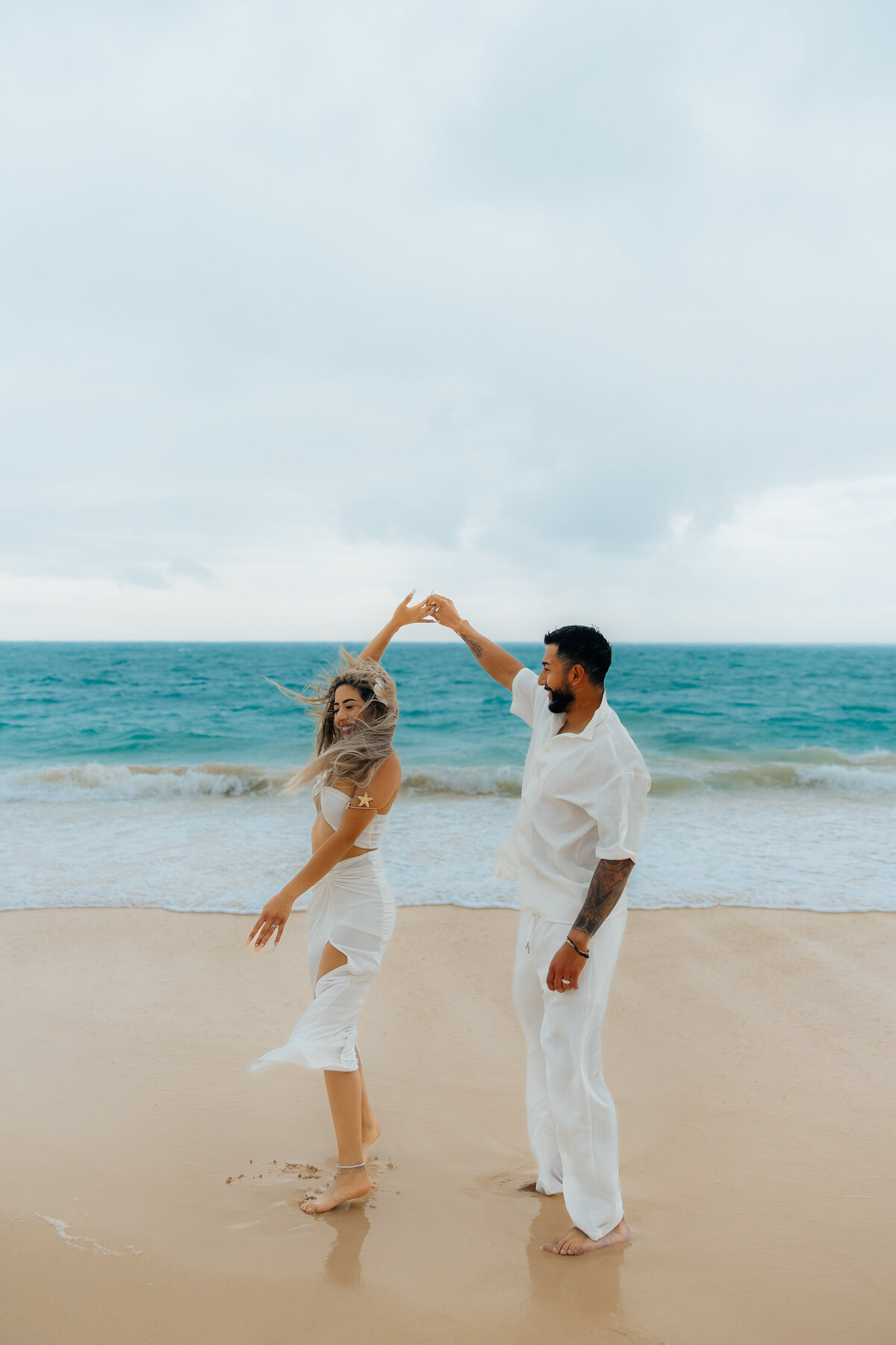 A couple dances barefoot on the shoreline during their rainy honeymoon photoshoot at Waimanalo Beach in Oahu.