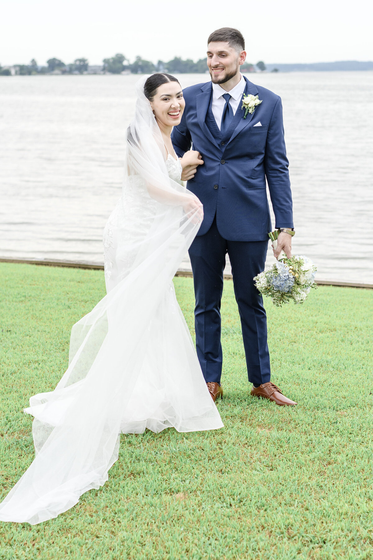 Bride smiling at the camera wrapped up in her veil and holding her husband.