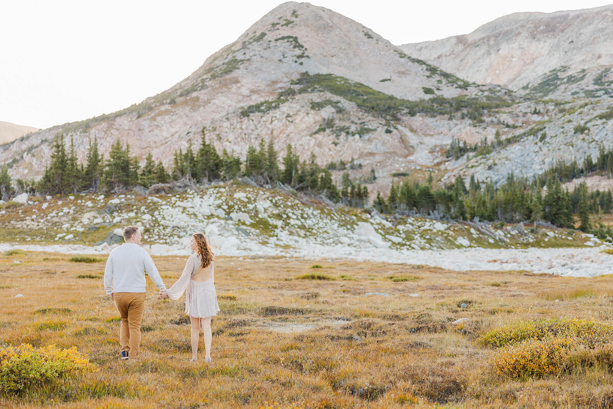 Couple walking hand in hand during their engagement session in the breathtaking Snowy Range Mountains, surrounded by stunning alpine scenery.
