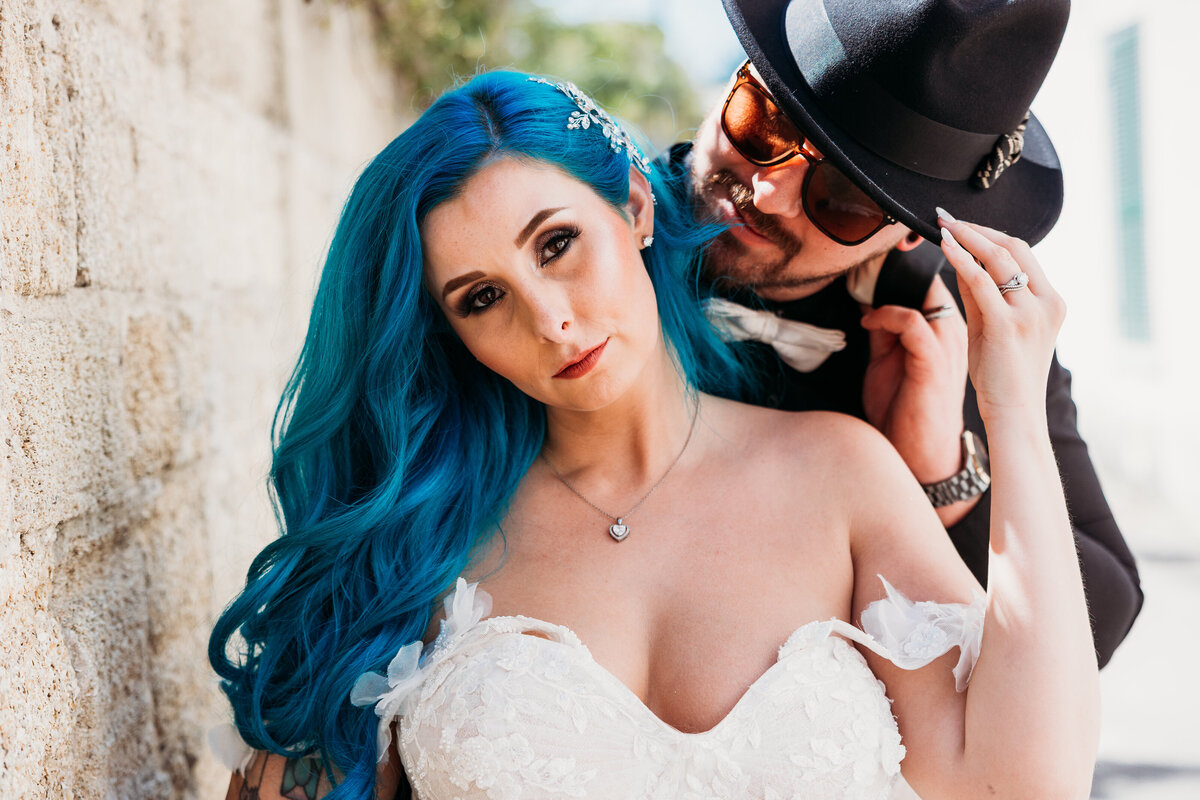 Bride with tattoos and blue hair leans in close to groom in a romantic alley moment during their alternative St. Augustine elopement.