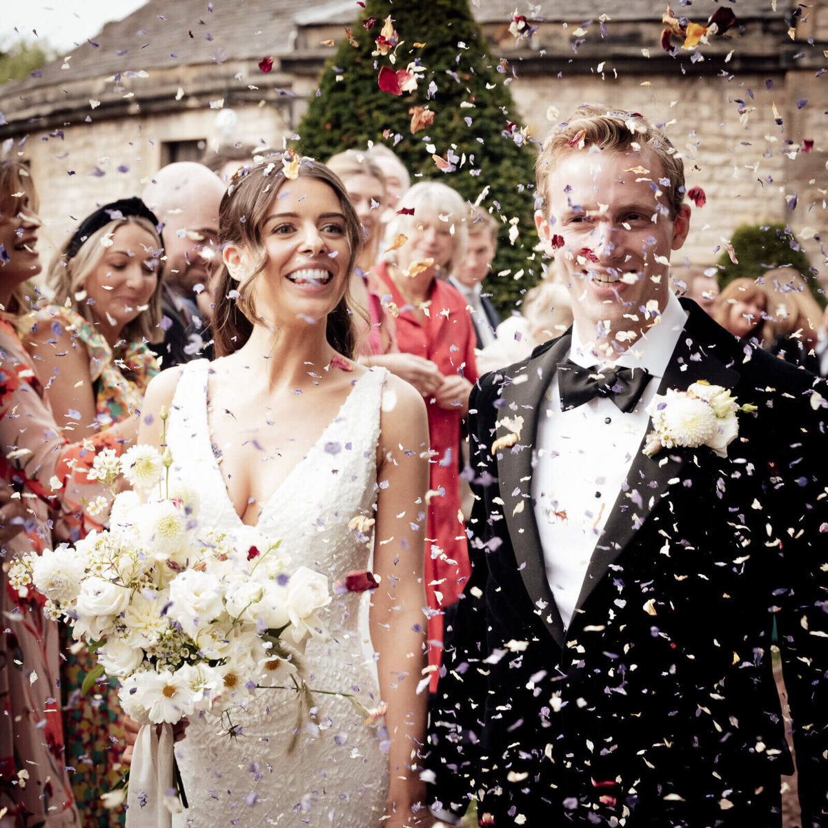 A bride and groom smile with joy as they are covered in confetti