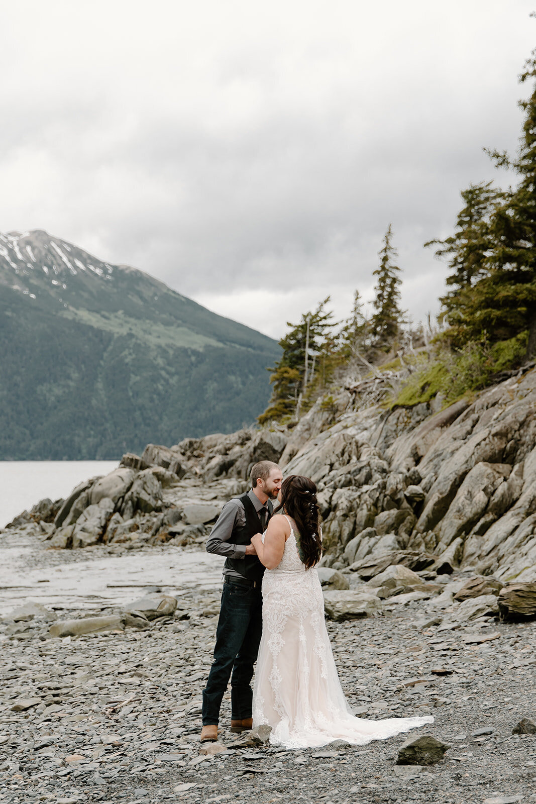 Elopement couple embraces on Alaska rock shoreline.