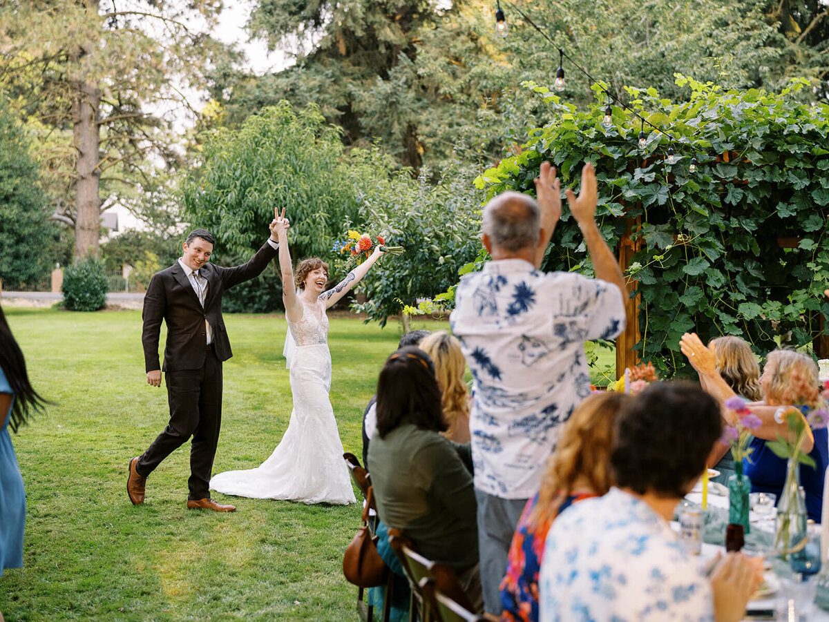 Bride and groom with arms raised as they join their guests in the reception. 